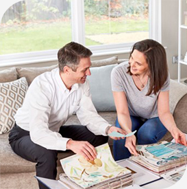 a man and woman sitting on a couch looking at a color swatch