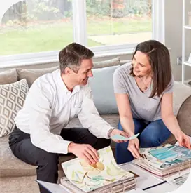 a man and woman sitting on a couch looking at a color swatch